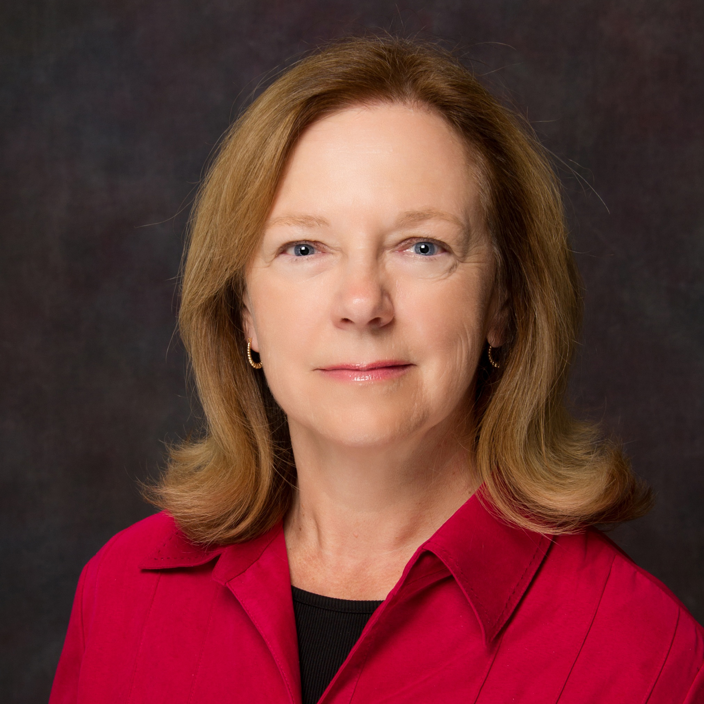 Heashot of Linda Waters, with shoulder-length light brown hair curled up at the ends, wearing a bright pink button-up shirt with a black shirt underneath.